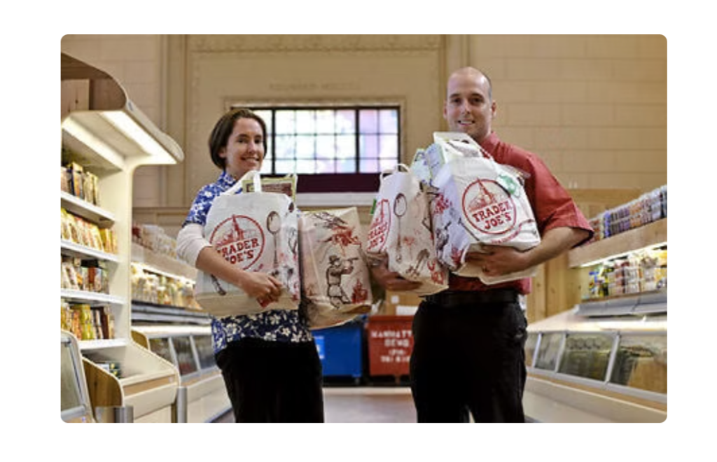 Screenshot of two Trader Joe’s employees holding grocery bags in a store aisle.